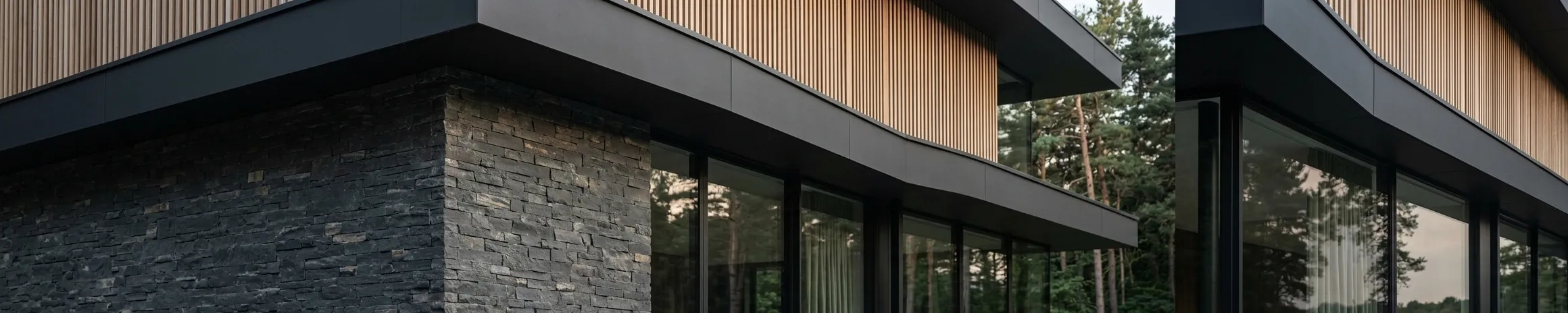 A close view of a building corner where vertical timber cladding meets a dark stone base beneath a deep, shadowed eaves line.